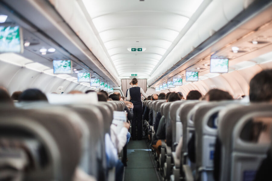 Airplane cabin interior featuring passengers seated and a stewardess in uniform serving in the aisle during a commercial flight