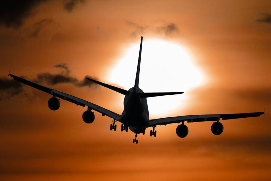 Airplane silhouette against dramatic sunset sky with vibrant colors and fluffy clouds.