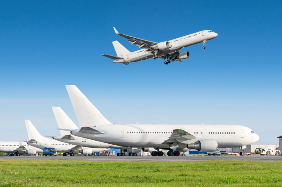 Passenger aircraft lined the airport, with one being towed and another landing beneath a clear blue sky