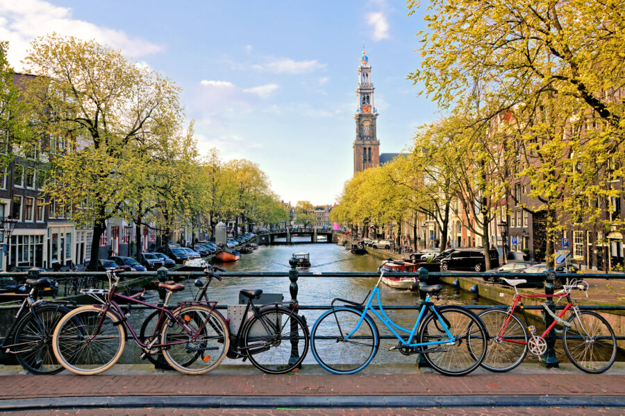 Bicycles parked on a bridge over Amsterdam's canals, with a church in the background, illuminated by late afternoon light