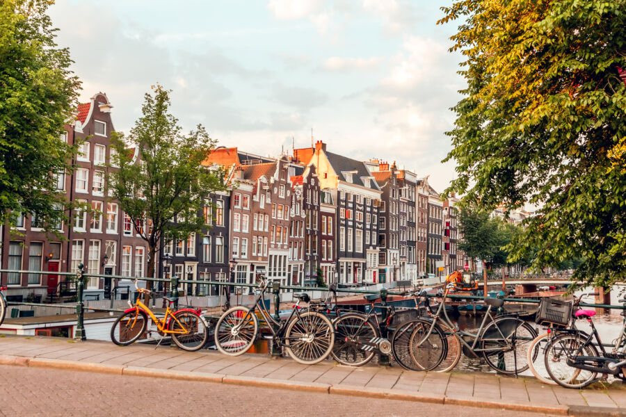 The sun rises over Amsterdam's canals and streets, creating a picturesque scene filled with soft light and vibrant colors