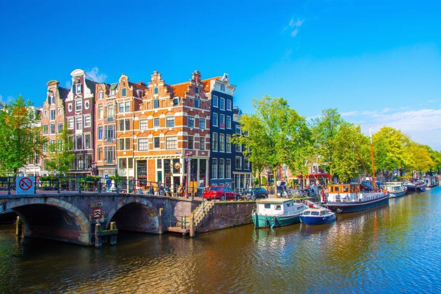 Scenic view of a tranquil Amsterdam canal, lined with historic buildings and lush greenery, reflecting the city's charm 