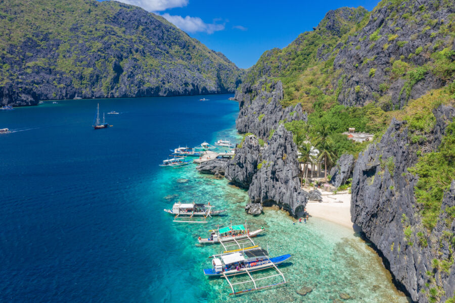 Beautiful coral reef and boats in a crystal-clear ocean, depicting the scenic allure of Matinloc Island, Bacuit Archipelago, Philippines