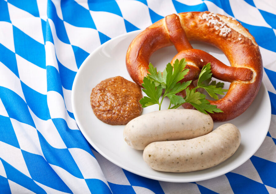 Close-up of Bavarian Weisswurst and pretzel on a white plate, showcasing the dish's textures and colors