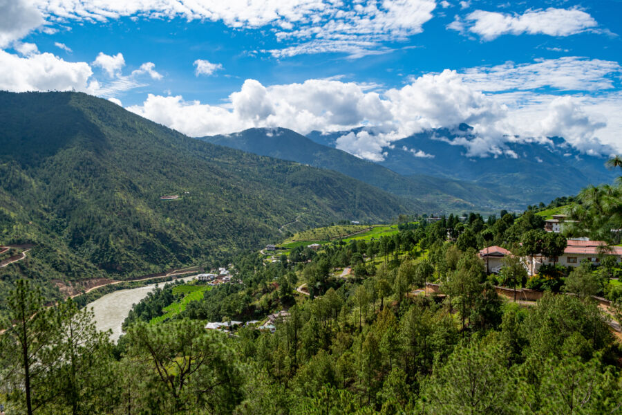 Scenic view of Bhutan's countryside, featuring lush green fields and majestic mountains under a clear blue sky