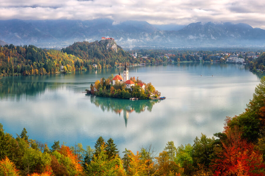 Aerial view of Bled Lake in Slovenia, showcasing the island church, Bled Castle, and the Julian Alps in autumn colors