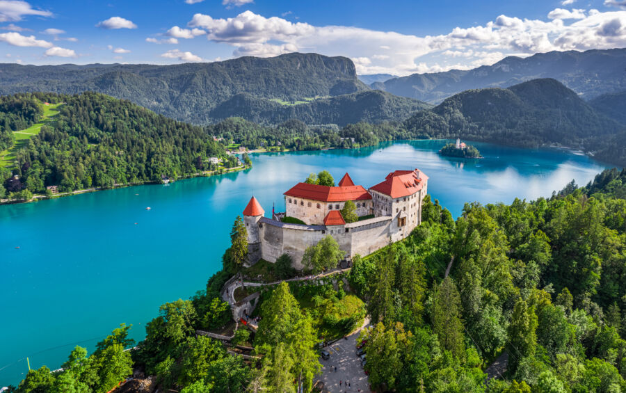 Aerial view of Bled Castle overlooking Lake Bled, the Church of the Assumption, and the Julian Alps on a summer day