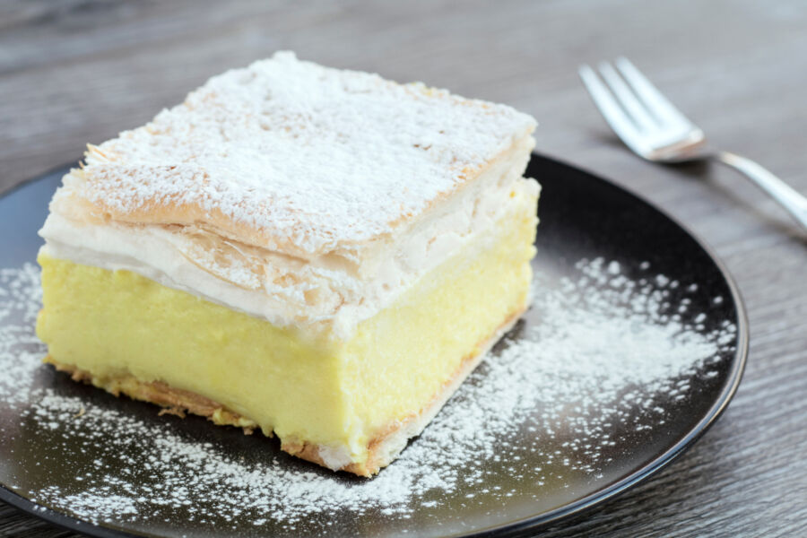 Bled Cream Cake or the kremšnita  with sugar icing displayed on a black plate atop a wooden table