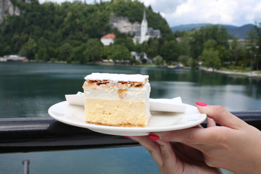 Slice of Bled Cream Cake, featuring layers of vanilla and custard cream, set against the scenic backdrop of Bled Lake, Slovenia