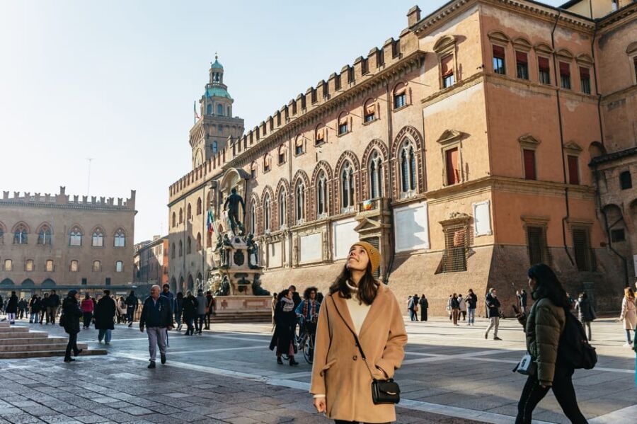 Woman in stylish coat enjoying lively Italian square with historic architecture and vibrant atmosphere.