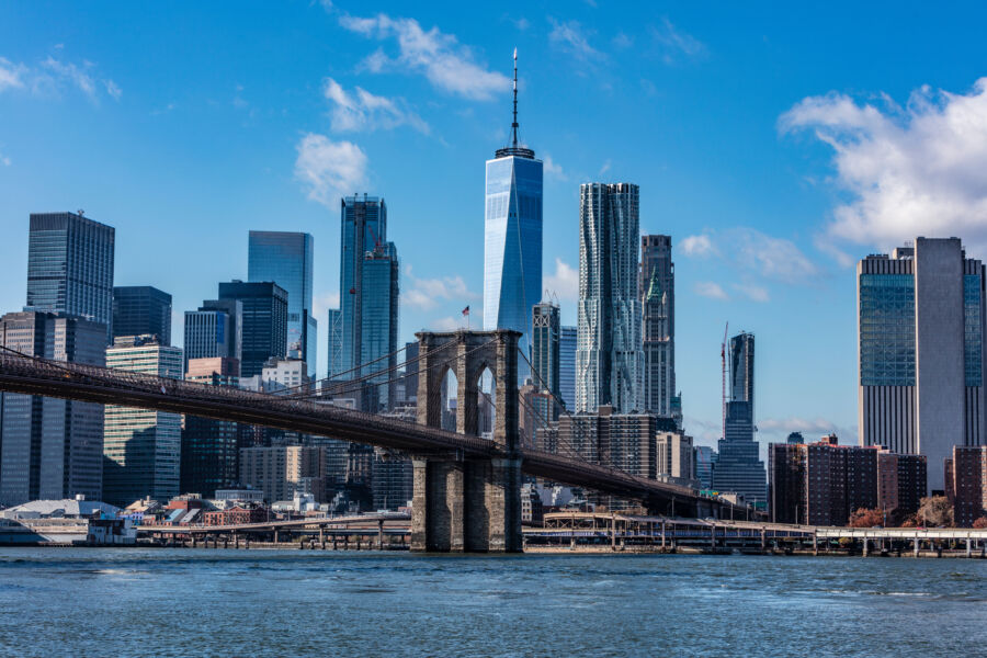 The Brooklyn Bridge spans across the water, framed by the impressive skyline of New York City, highlighting urban beauty