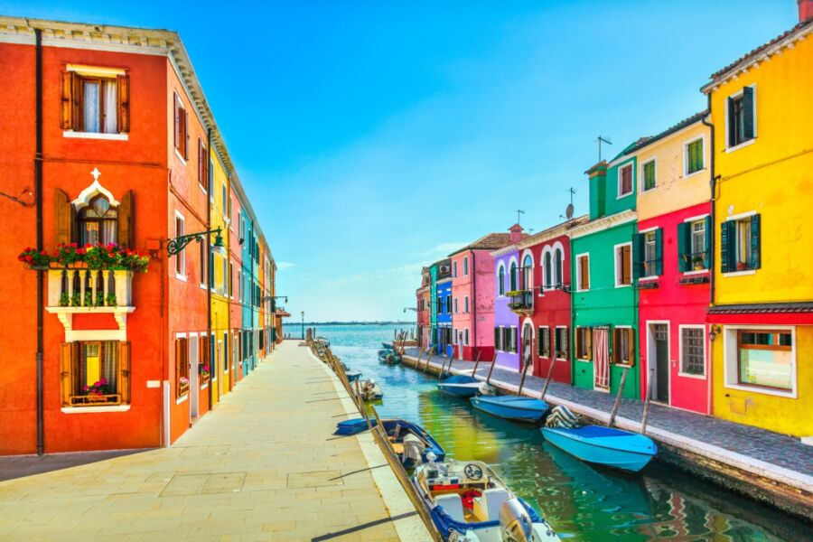 Colorful houses line the canal on Burano Island, Venice, with boats adding to the scenic beauty of this Italian landmark