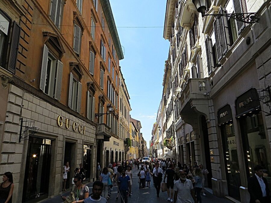 Bustling urban street with luxury boutiques, diverse pedestrians, and elegant historic architecture.