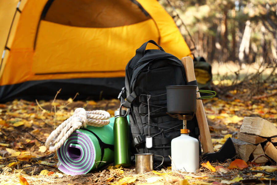 Camping tent alongside a survival kit and camping essentials nestled in an autumn forest