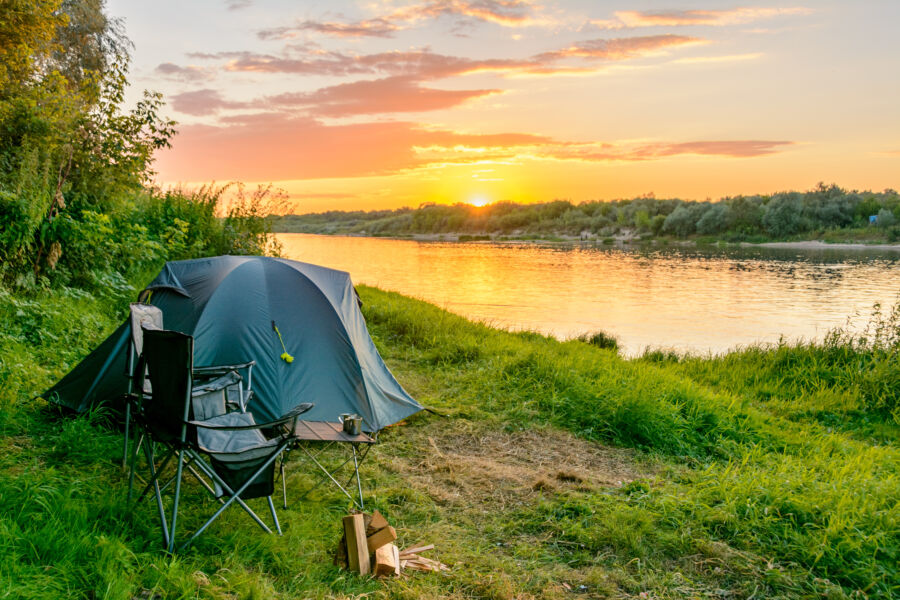 Camping tent set up in a forest near a serene river, surrounded by lush greenery and natural beauty