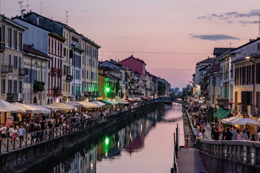 Urban canal scene with vibrant nightlife, colorful buildings, and lively crowd at sunset.