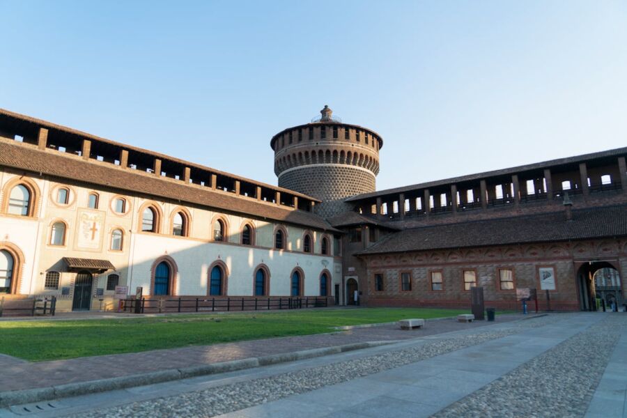 Historic medieval castle tower with crenellations, arched windows, and cobblestone path under clear sky.