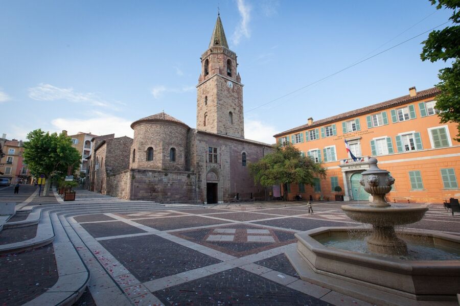 Historic European square with medieval church, cobblestones, fountain, and colorful buildings.