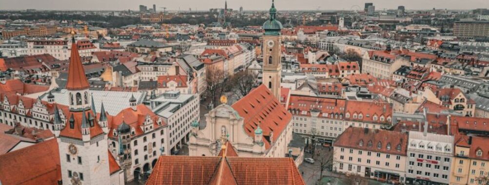 Panoramic view of Munich with diverse architecture, red rooftops, clock tower, cloudy sky.