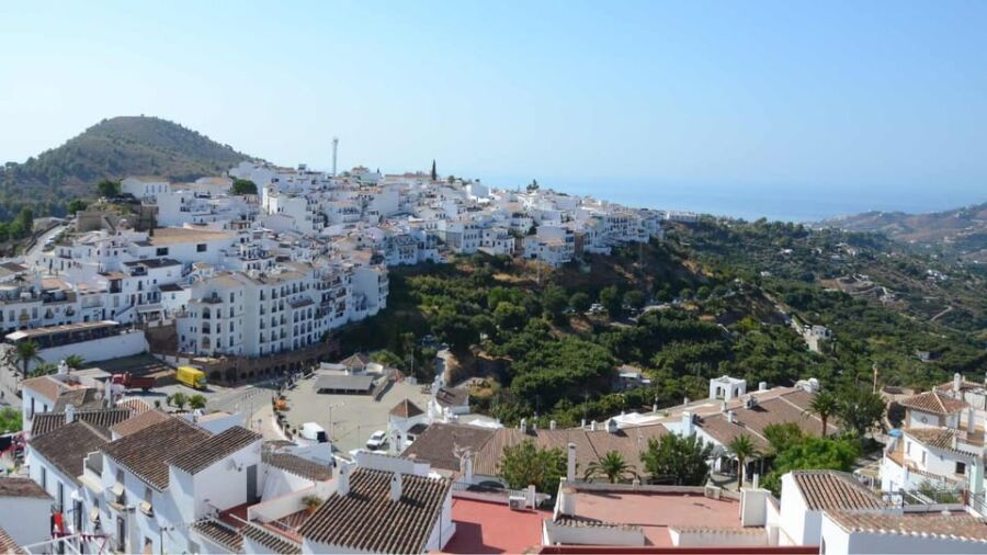 Whitewashed Andalusian village with terracotta roofs, Mediterranean views, lush greenery, and clear skies.