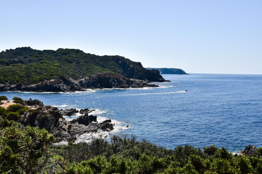 Serene coastal landscape with rocky shore, lush greenery, and a boat on calm blue waters.