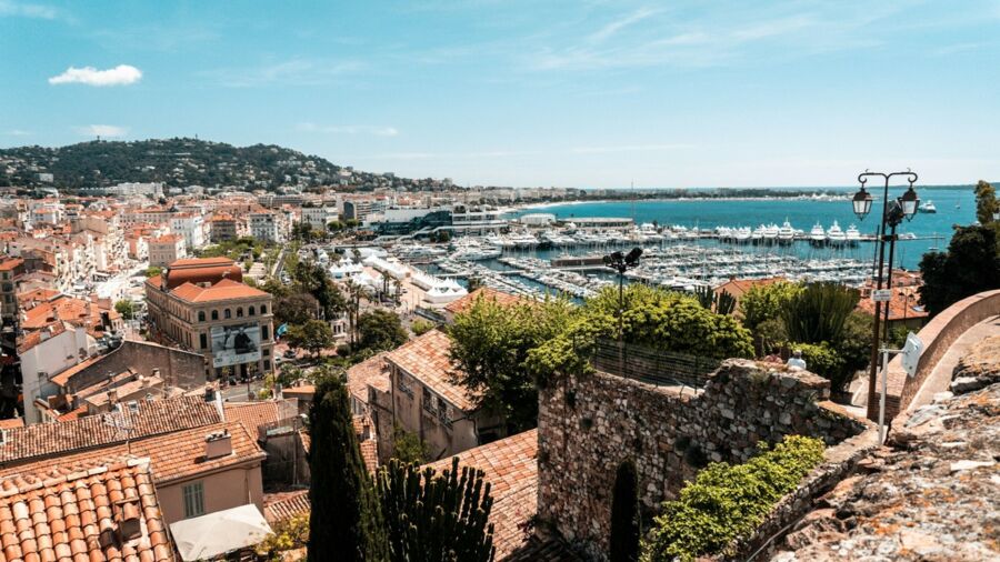 Panoramic view of a coastal town in South France, featuring harbor, terracotta roofs, and mountains.