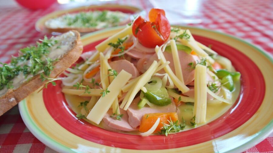 Colorful salad with ham, vegetables, cheese, microgreens, and bread on a vibrant plate.