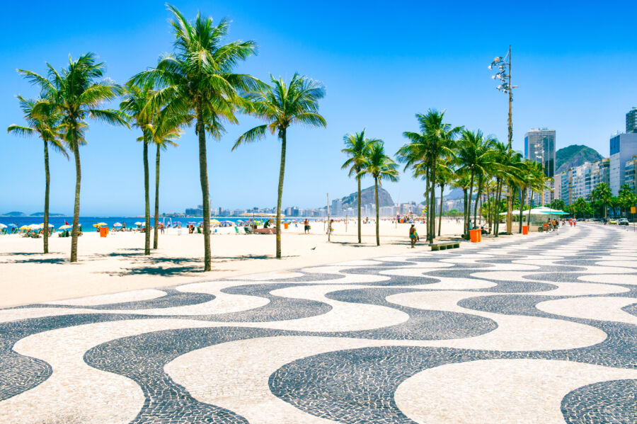 Morning scene at Copacabana Beach featuring a curving tile boardwalk, palm trees, and the skyline of Rio de Janeiro