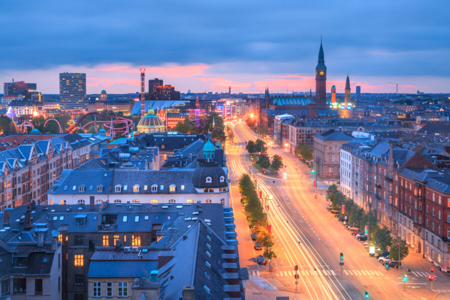 Twilight cityscape of Copenhagen, featuring light trails on H.C. Andersen Boulevard and the City Hall clock tower illuminated at night