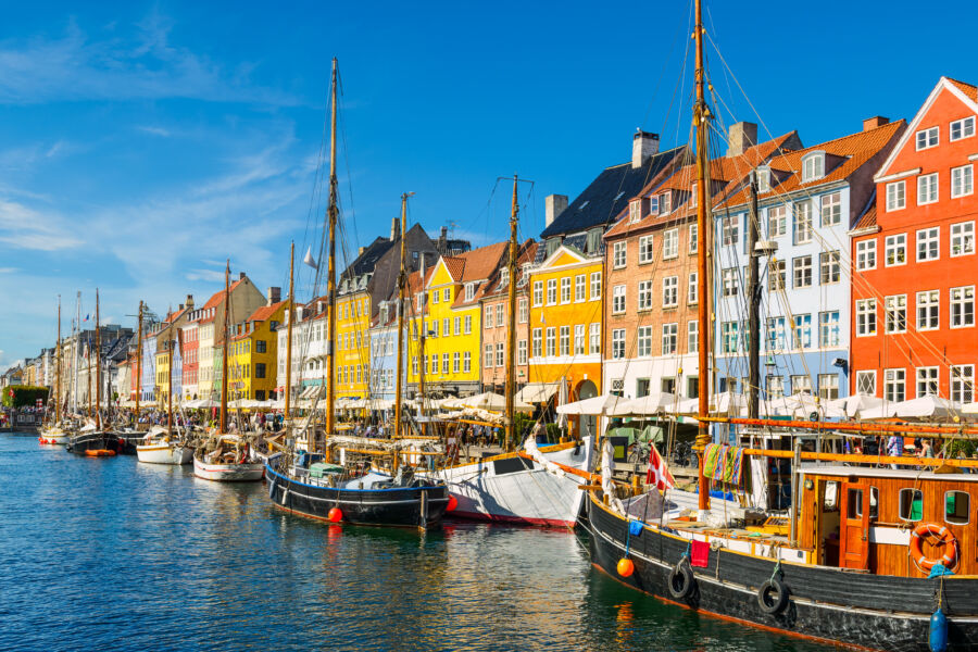 Sunny day at Nyhavn harbor in Copenhagen, Denmark, with colorful facades reflecting in the canal