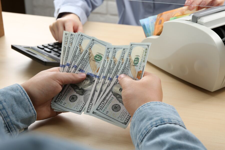 Close-up of hands counting money on a table, with various bills and coins arranged neatly