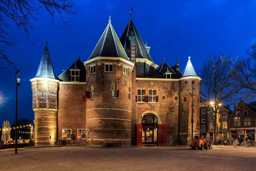 Exterior view of De Waag building in Amsterdam at night, illuminated against a dark sky, showcasing its historic architecture