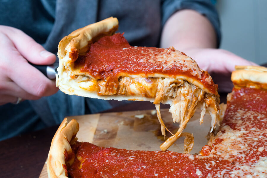 Hand getting  a Chicago deep-dish pizza topped with cheese and tomato sauce