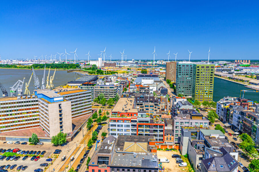 Panoramic aerial view of Antwerp's Eilandje neighborhood, featuring the port area, canals, and windmills against the skyline