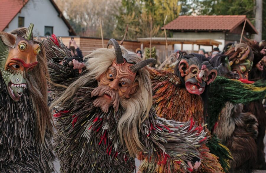 Traditional cultural festival with performers in elaborate masks and costumes, vibrant rural setting.