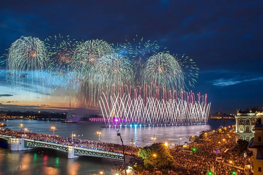 Fireworks over river during White Nights Festival; vibrant twilight celebration with crowd and reflections.