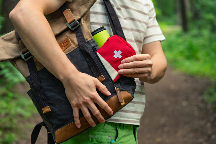 Close-up view of an individual pulling a first aid kit from a backpack while hiking on a forest trail