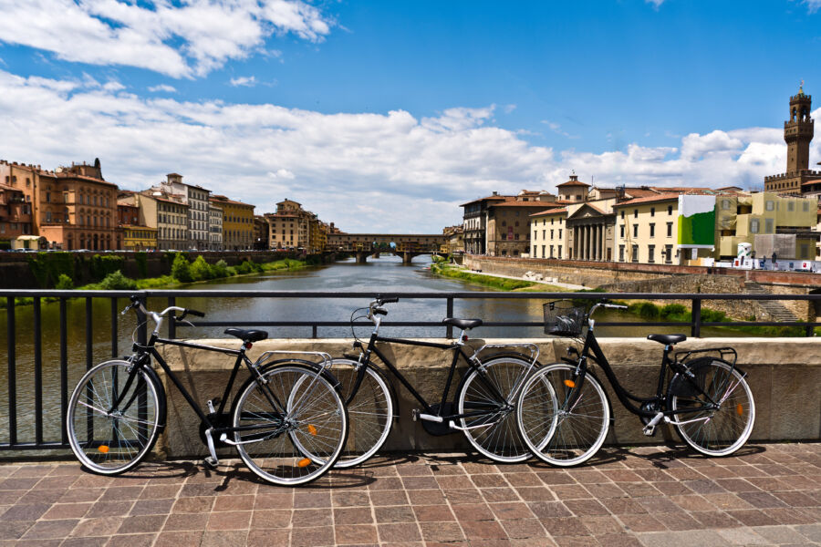 Bikes lined up on a bridge overlooking the River Arno in Florence, Italy, showcasing a scenic urban landscape