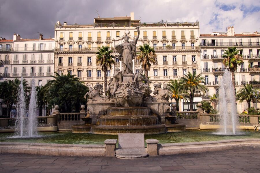 Grand urban fountain with statue, lively water jets, elegant architecture, and tropical palm trees.