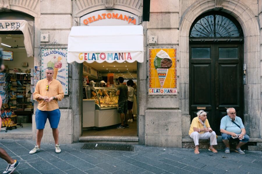 Gelato shop street scene with customers enjoying gelato on a sunny day.