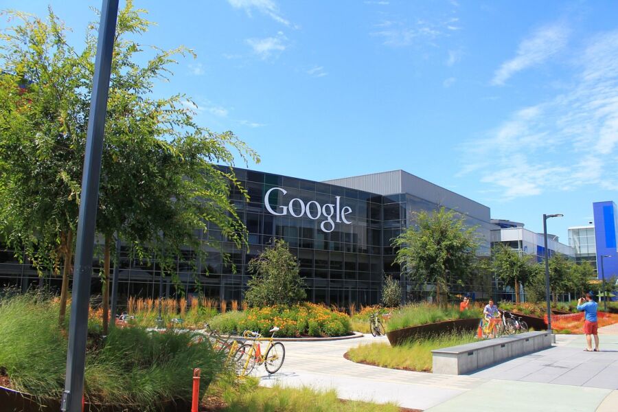 Modern Google building with glass façade, green landscaping, bicycles, and active social atmosphere.