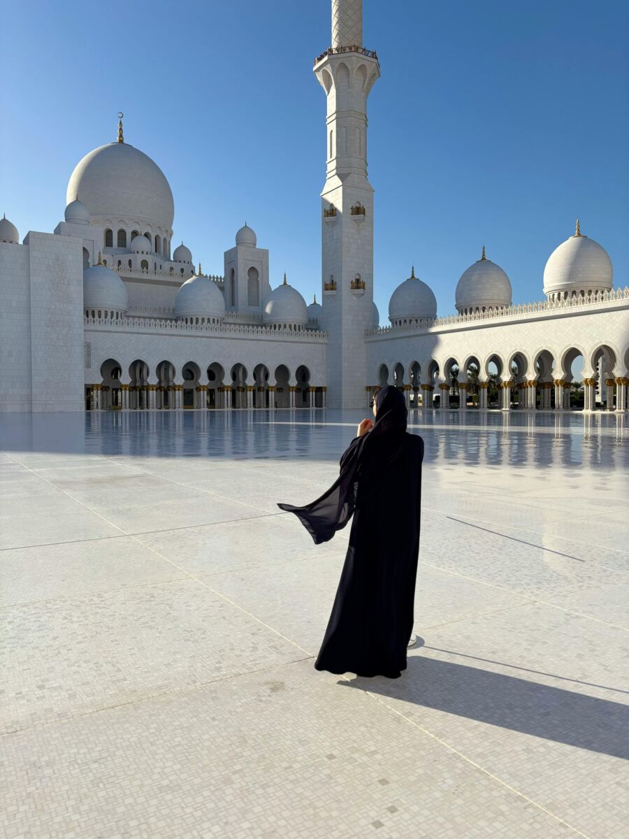 Serene courtyard view of Sheikh Zayed Grand Mosque with lone figure and stunning architecture.