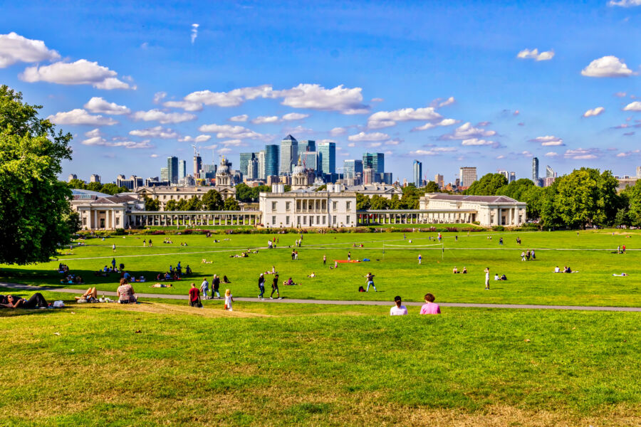 Scenic view of Canary Wharf from Greenwich Hill, framed by the vibrant greenery of Greenwich Park in London, England