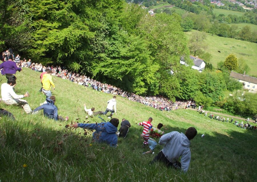 Cheese rolling competition on steep hill in Gloucestershire with excited participants and spectators.