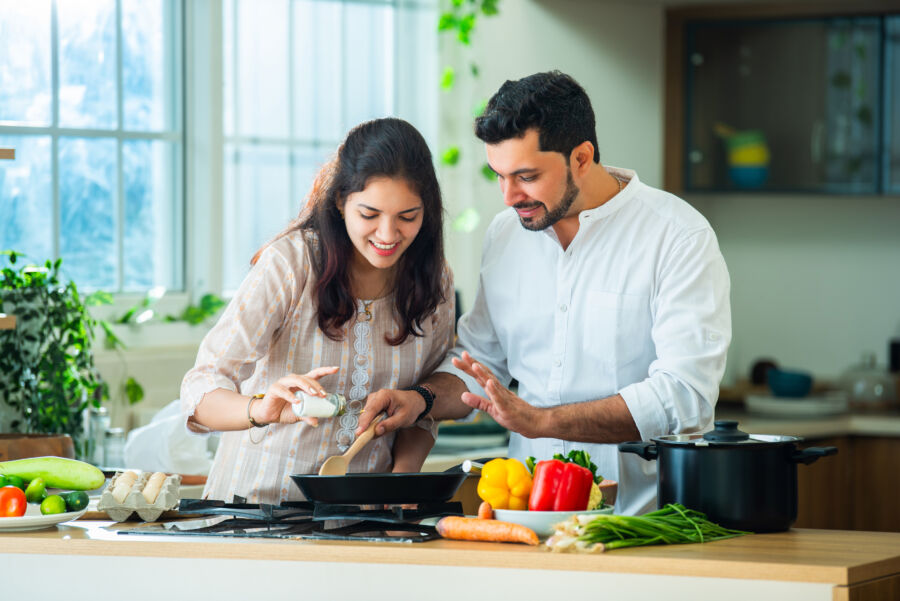 Asian Indian young newly married couple spend time together trying new recipe in kitchen at home, enjoying cooking meal or breakfast 