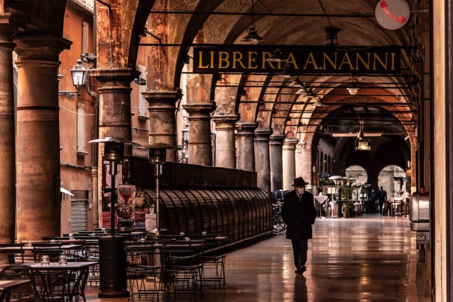 Serene Italian arcade with bookstore, architectural details, solitary figure, and atmospheric charm.