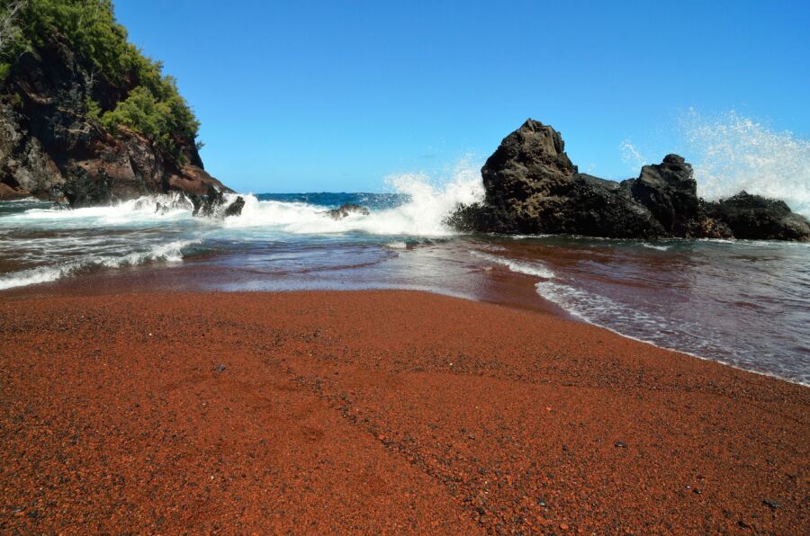 The striking red sands of Kaihalulu beach in Maui, Hawaii, framed by vibrant greenery and the azure ocean waves