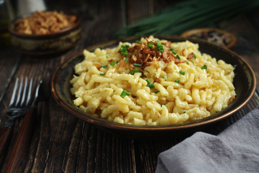 Close-up of käsespätzle, a hearty cheese noodle dish, served on a plate with melted cheese and herbs visible