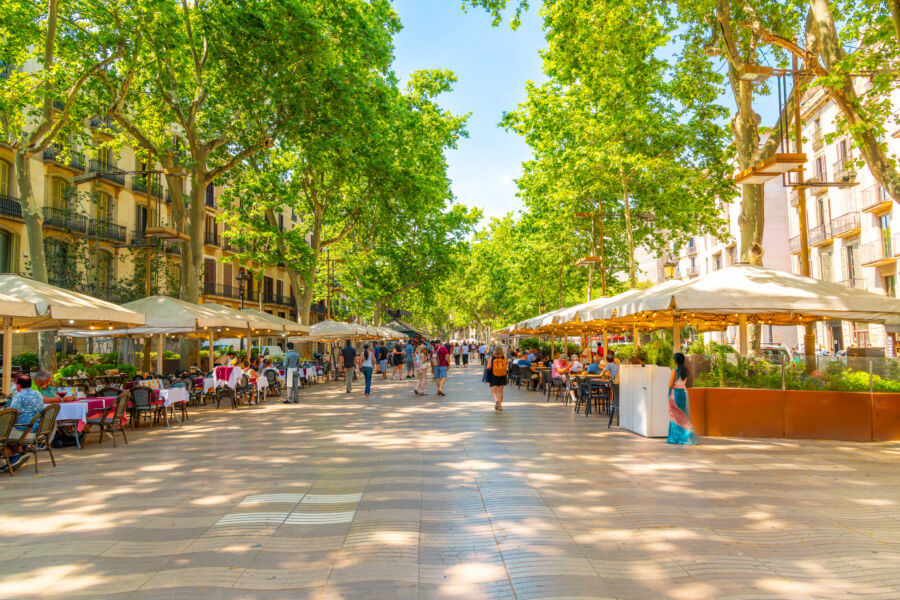 Tourists stroll by sidewalk cafes along La Rambla in the historic Mediterranean city of Barcelona, Catalonia, Spain