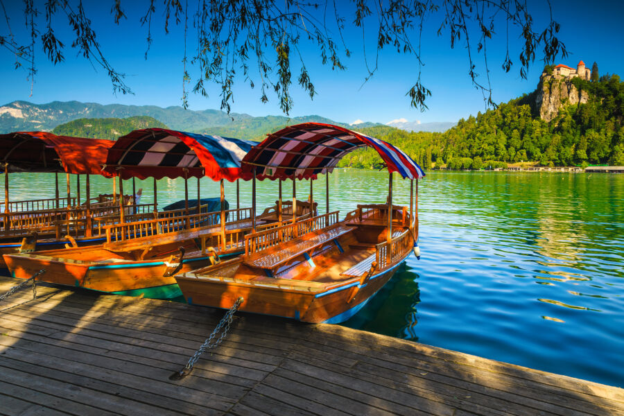 Scenic view of wooden Pletna boats on Lake Bled, with Bled Castle perched on a hill in the background, Slovenia